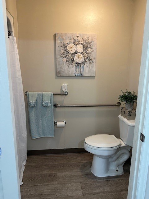 A bathroom with a toilet, a towel, and a painting on the wall at Spring Arbor of Rocky Mount